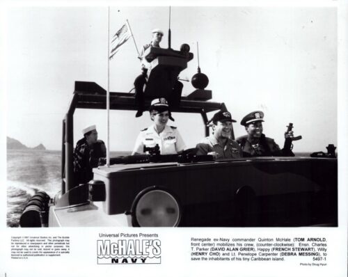 Black-and-white photo of a U.S. Navy crew on a patrol boat, smiling and posing with a flag on deck; publicity still for McHale's Navy.