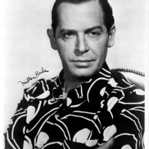 Portrait of comedian Milton Berle with arms crossed, wearing a bold patterned shirt and a calm, confident expression.