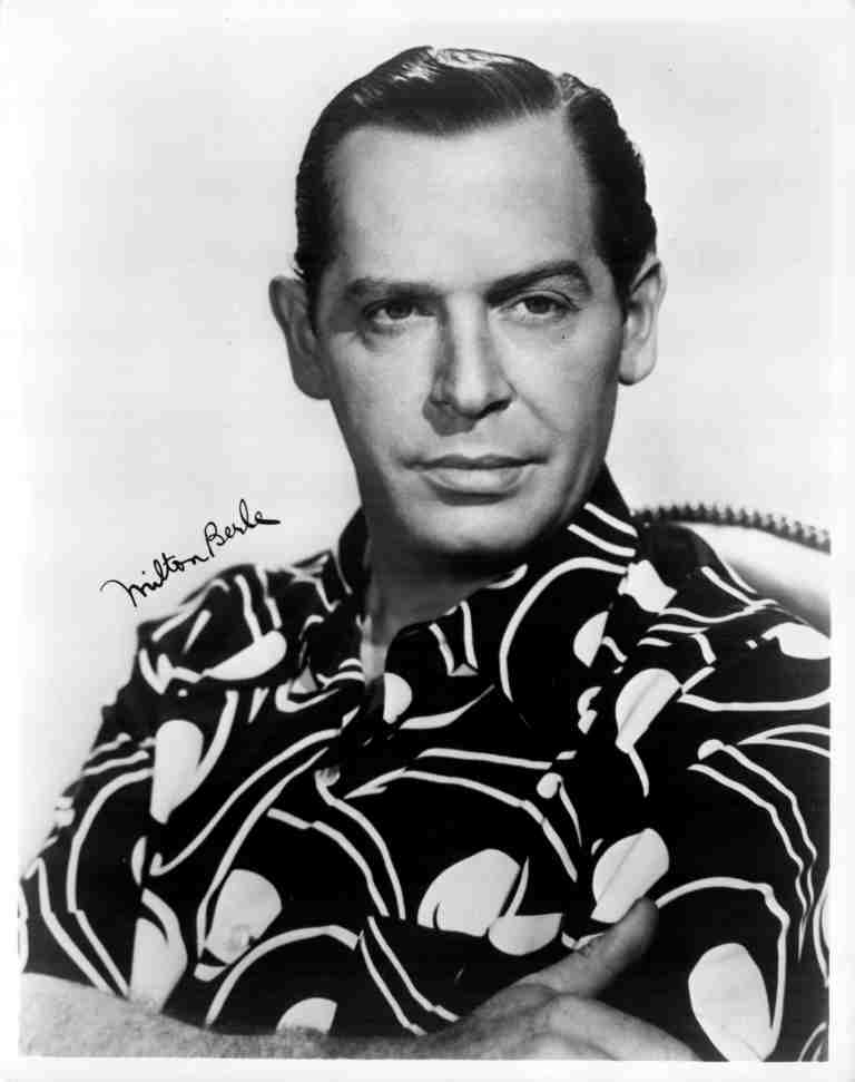 Portrait of comedian Milton Berle with arms crossed, wearing a bold patterned shirt and a calm, confident expression.