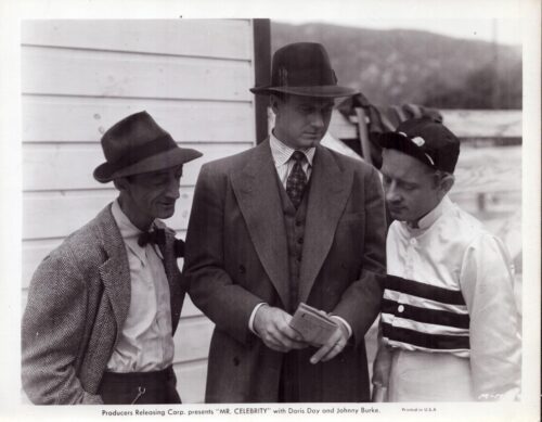 Promotional still for the film Mr. Celebrity, showing three men in fedoras and suits gathered around a newspaper.