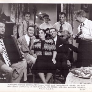 Black-and-white photo of a mid-20th-century living-room band: accordion player, bass, and guitarists surround a smiling couple seated in the center.