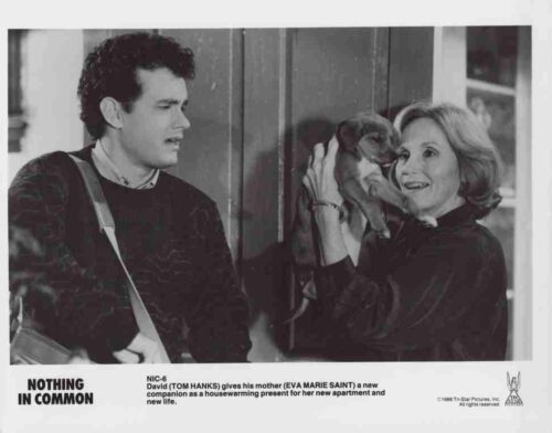 Black-and-white still from the film Nothing in Common; a man with a shoulder bag glances at a woman holding a small dog.