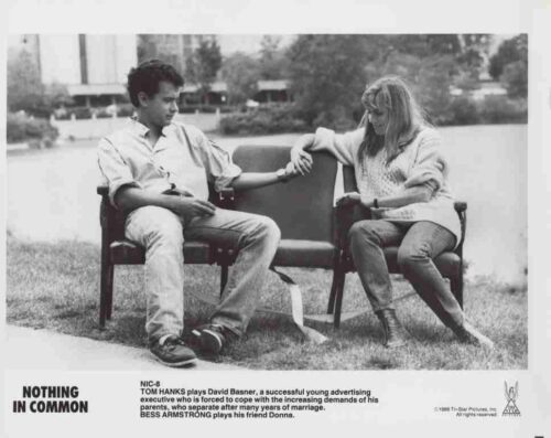 Black-and-white photo of a young man and woman sitting on separate chairs outdoors by a lake, holding hands and looking at each other; movie poster text reads 'Nothing in Common'.