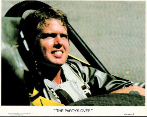 Pilot in a cockpit wearing a gray flight suit and headset, smiling; caption at bottom reads 'THE PARTY'S OVER'