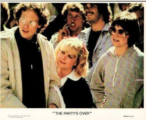 Group of young adults at a party, smiling and looking to the left; a blonde woman stands near center, with others in casual 80s attire. Caption reads 'The Party's Over'