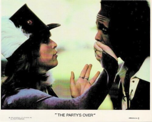 A woman in a hat pulls back a man’s sleeved mask, revealing his face in a tense moment from a poster. A woman reaching toward a man’s masked face on a vintage movie poster with the caption 'THE PARTY'S OVER'. Close-up of a woman lifting a cloth mask off a man, as part of a film poster scene. Wom an in a hat touches a man’s masked face in a dramatic poster for 'The Party's Over'. Film poster moment: a woman pulls away a mask from a man's face, signaling exposure or revelation.