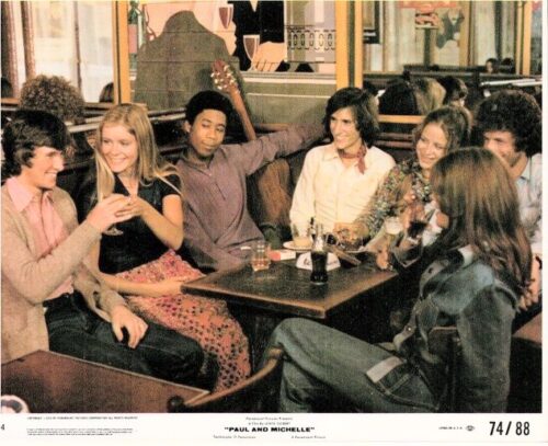 A group of seven young adults gathered around a booth at a retro cafe, smiling and chatting with drinks on the table.