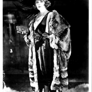 Black-and-white photo of a glamorous woman in a satin dress, pearls, fur wrap, and cloche hat, holding a clutch.