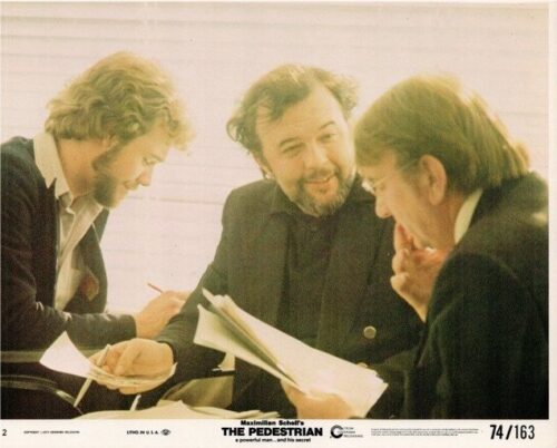 Three men in suits review documents together, smiling and discussing a stack of papers on a table.