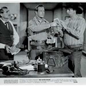 Three men in Western attire count money around a desk with a safe open and scattered cash, a cowboy hat resting on the table.