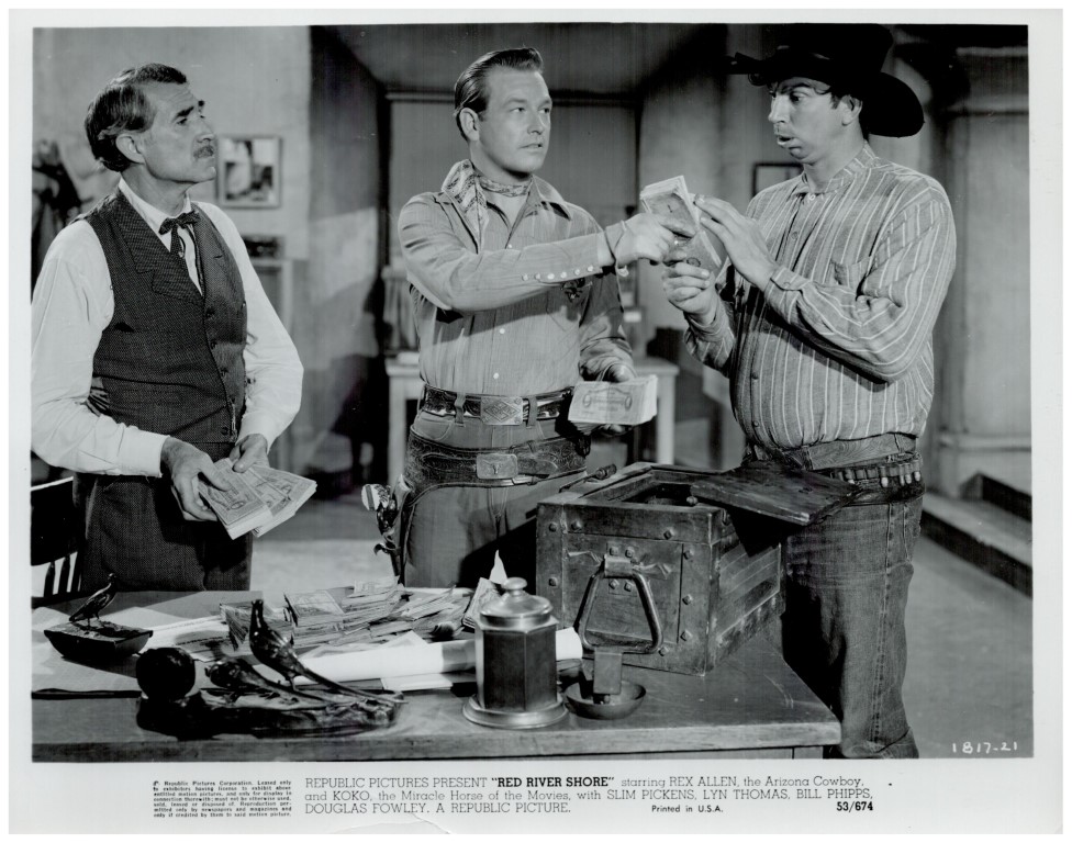 Three men in Western attire count money around a desk with a safe open and scattered cash, a cowboy hat resting on the table.