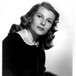 Black-and-white portrait of a woman with wavy hair, wearing a dark outfit and a white collar, looking at the camera.