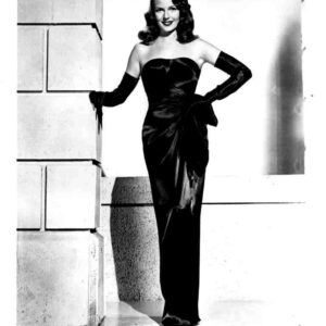 Rita Hayworth in a strapless black gown with long gloves, posing against a stone wall for a classic film still from Gilda (1950).