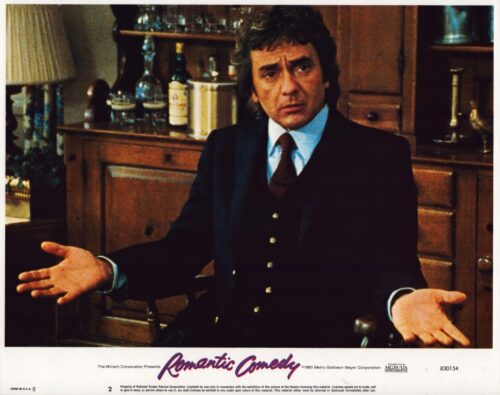 Man in a dark three-piece suit gestures with open hands on a vintage poster for the film Romantic Comedy.