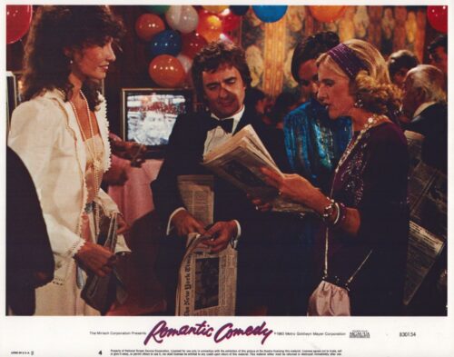 Man in a tuxedo reads a newspaper at a festive party as two women in evening wear gaze at it, balloons overhead in a mid-1980s setting.