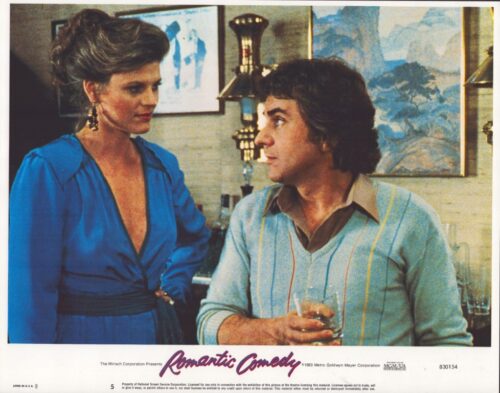 Woman in a blue dress talks with a man in a light blue striped sweater at a bar, the man holding a glass.