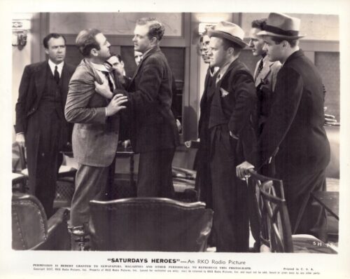 Black‑and‑white photo of men in 1930s suits; two men argue, one grabbing the other's lapels as others watch in a formal room.