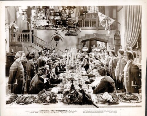 Black-and-white film still: a long banquet table crowded with diners, flanked by officers in uniform in a grand hall.