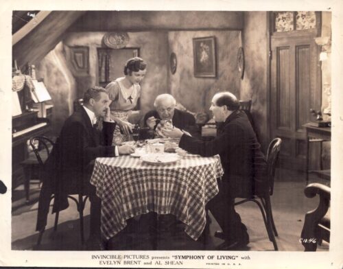 Four people gather around a round table with a checkered tablecloth as a waitress serves in a vintage parlor setting.