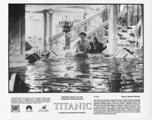 Still from Titanic: a man and woman wading through flooded grand lobby with a staircase and debris in the background.
