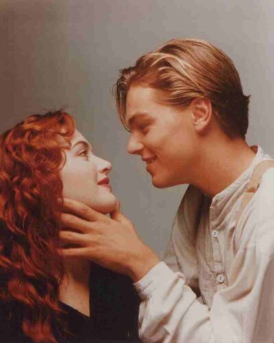 A man and woman lean in close, smiling, as the man gently holds the woman's chin for a kiss.
