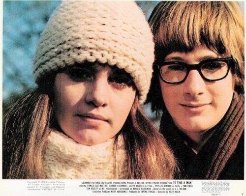 Two young women posing outdoors in winter clothing, one wearing a knit hat and scarf, the other with glasses and a hooded coat.