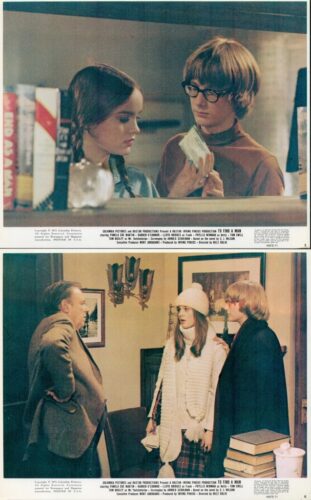 Two young people in a bookstore-like setting; a man with glasses shows a card to a woman who looks at it, shelves visible in the background to the left.