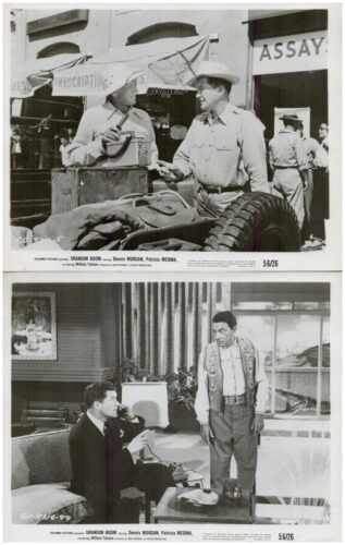 Two men in cowboy hats talk beside a car and crates on a street-set from a 1950s Western film, with an 'ASSAY' storefront in the background.