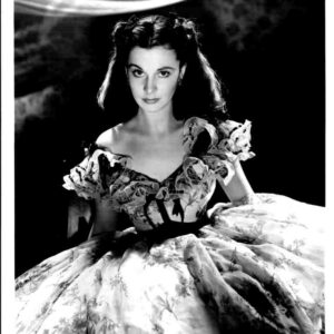 Black-and-white portrait of a woman in an elaborate ball gown with floral embroidery, looking directly at the camera.