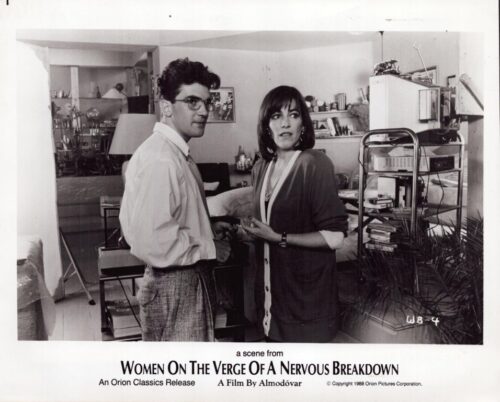 Two characters converse in a cluttered living room, with shelves and equipment in the background; a scene from Women on the Verge of a Nervous Breakdown.