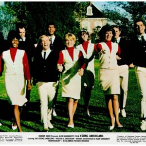 Group of young adults in vintage uniforms walking toward the camera on a sunny green lawn, smiling together.