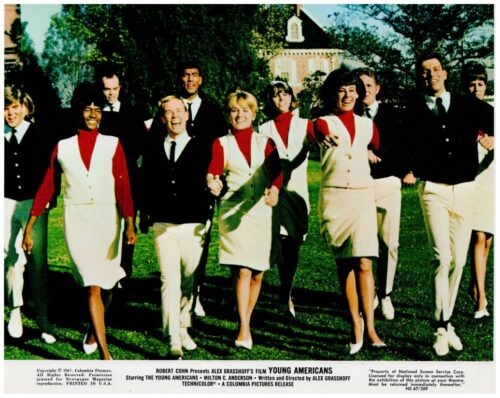 Group of young adults in vintage uniforms walking toward the camera on a sunny green lawn, smiling together.