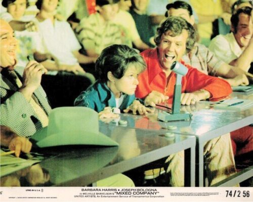 Panel scene at a press conference: a young girl leans toward the microphone while a man in red smiles beside her, others watching in the background.