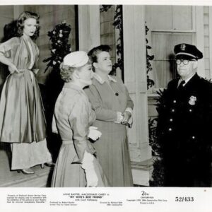 Two women in 1950s dresses converse with a uniformed police officer on a porch as a third woman watches in the background.