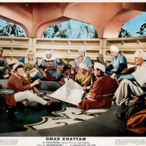 Group of men in turbans and robes sit in a courtyard, gathered around a low table with a large map, discussing plans.