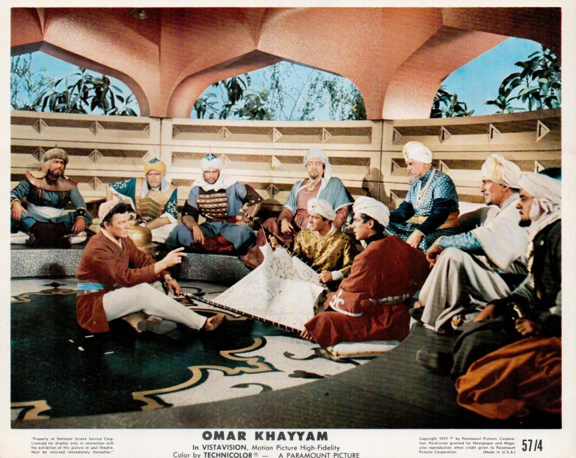 Group of men in turbans and robes sit in a courtyard, gathered around a low table with a large map, discussing plans.