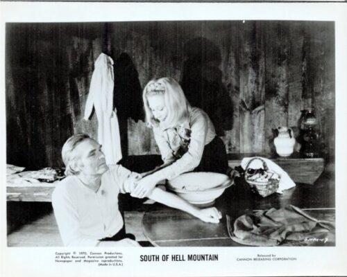 Black-and-white still from South of Hell Mountain: a man sits at a counter as a woman leans over and offers something from a bowl on the counter.