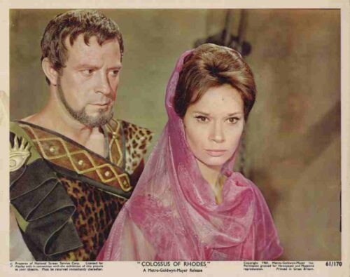 Movie still from Colossus of Rhodes: a rugged warrior in leopard-print armor beside a woman in a pink veil.