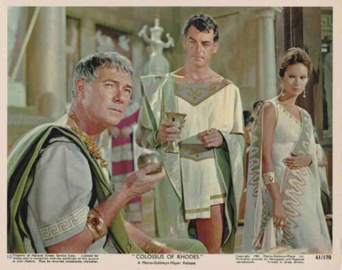 Three people in Greco-Roman robes; an older man seated with a goblet, a younger man holds a chalice, and a woman stands nearby in a palace setting.