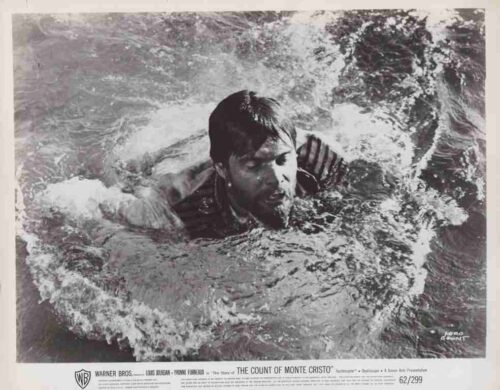 Black-and-white still of a man swimming through choppy water, his head above waves, from The Count of Monte Cristo promotion.