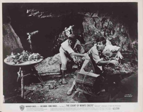 Two men in a rocky cave inspect a large treasure chest as one helps the other; film still from The Count of Monte Cristo.