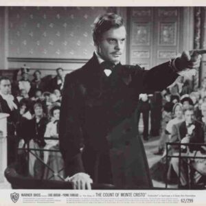 Black-and-white film still: a man in a tuxedo points to the right from a podium, addressing a crowded room; The Count of Monte Cristo poster.