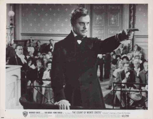 Black-and-white film still: a man in a tuxedo points to the right from a podium, addressing a crowded room; The Count of Monte Cristo poster.