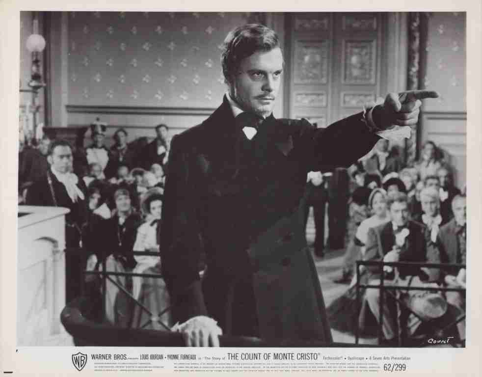 Black-and-white film still: a man in a tuxedo points to the right from a podium, addressing a crowded room; The Count of Monte Cristo poster.