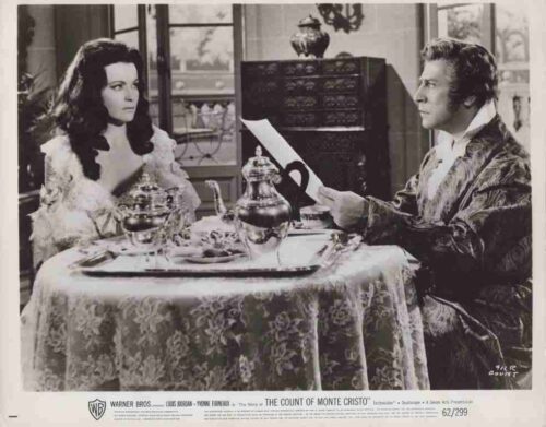 Black-and-white scene from The Count of Monte Cristo: a man in a velvet robe reads a letter to a woman in lace at a dining table with ornate tea service.
