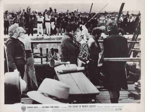 Still from The Count of Monte Cristo on a ship deck: a couple kisses while a crowd watches the scene in the background.