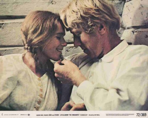 A man in a white shirt applies lipstick to a smiling woman as they lean foreheads together.
