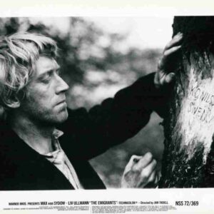 Black-and-white still of Max von Sydow as a man with light hair, touching a tree trunk and carving/writing on it outdoors in a somber scene from The Emigrants