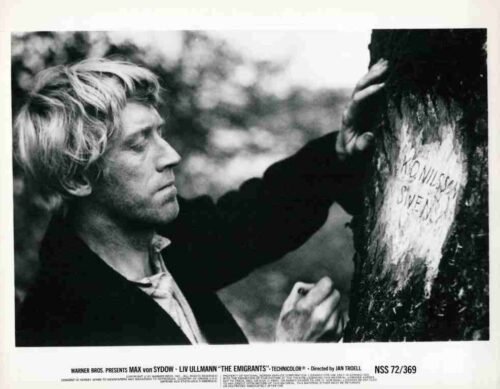 Black-and-white still of Max von Sydow as a man with light hair, touching a tree trunk and carving/writing on it outdoors in a somber scene from The Emigrants