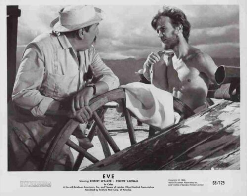 Black-and-white still from the 1960 film Eve: two men on a ship's deck at a steering wheel, one shirtless and talking to the other in a hat.